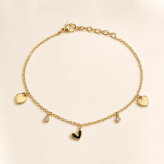 One anklet of yellow-gold-coloured metal with a bright polished finish. It is a single-strand, fine-gauge cable chain of small oval links. The full chain run measures roughly 30 times the width of its largest component (the plain heart charms), and a short extender of larger oval links, about one-fifth the main chain's length, attaches at one end. A working lobster clasp is present at the opposite end, giving one clasp and one extender; no terminal tag is visible.