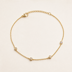 One anklet: a yellow-gold-tone, bright-polished flexible ankle chain made as a single fine cable-link strand of small oval links. The main chain run is approximately eighty times the width of the largest station; the adjustable extender is about one quarter of the main-chain length. A working lobster-claw clasp is visible.