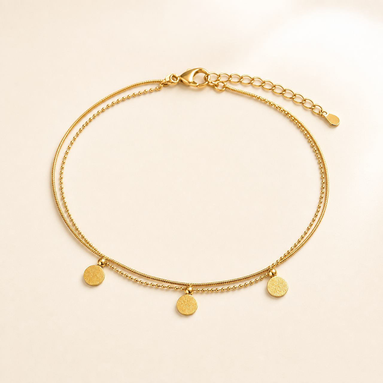 One anklet in yellow-gold-tone metal with a polished finish. It is built as two parallel fine strands joined at shared end fittings: a smooth snake-type chain and a slightly heavier beaded/ball chain of small linked spheres, both of fine gauge. The chain run is roughly twenty times the width of the largest component, and the short extender at the far end is about one-sixth of the main chain length.