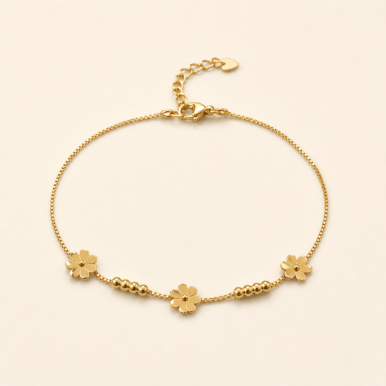 One anklet in yellow-gold-toned metal with a bright polished finish. It is a single-strand fine box chain of small, uniform square links, forming a closed flexible loop with no branches. The chain run measures roughly 25 times the width of the largest component (a flower charm); the curb-link extender chain is about one-fifth the length of the main chain. A working lobster clasp is visible at the junction.