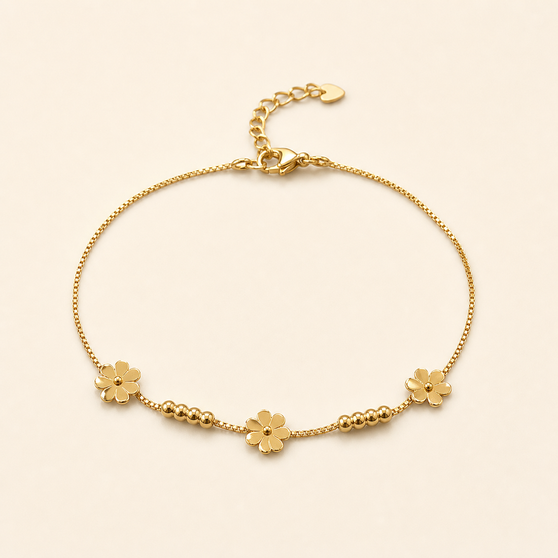 One anklet in yellow-gold-toned metal with a bright polished finish. It is a single-strand fine box chain of small, uniform square links, forming a closed flexible loop with no branches. The chain run measures roughly 25 times the width of the largest component (a flower charm); the curb-link extender chain is about one-fifth the length of the main chain. A working lobster clasp is visible at the junction.