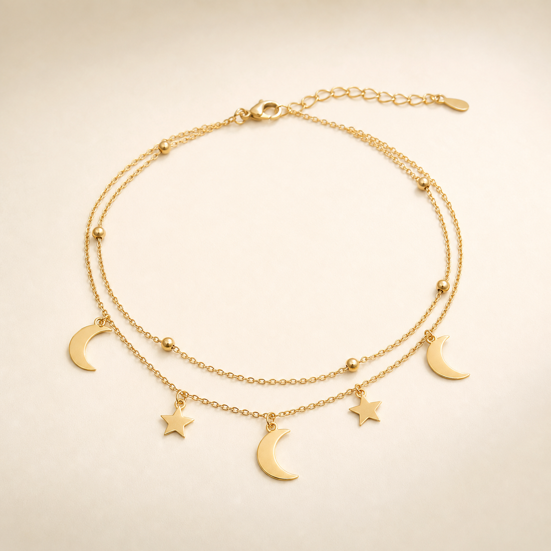 One anklet in yellow-gold-toned metal with a polished finish. It is built as two parallel fine cable-chain strands of small-gauge oval links joined at a single lobster clasp, giving a double-strand topology along most of the chain run. The full chain run is approximately 16 to 18 times the width of the largest crescent-moon charm, and the short extender chain near the clasp is roughly one-tenth of the main chain length.
