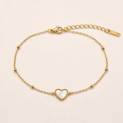 One anklet in yellow-gold-tone metal with a polished finish. It is a single fine cable chain of small oval links, one continuous strand. From the clasp end: a lobster clasp, working and visible, attaches to a short section of chain; a long extender chain of larger curb-style links, roughly one quarter the main chain's length, ends in a flat rectangular terminal tag, one tag total. The main chain run is approximately 20 times the width of the largest component, the heart charm.