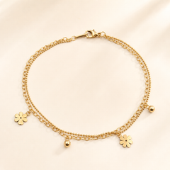 One anklet in yellow-gold-toned metal with a polished finish. It is a double-strand construction: one strand is a medium-gauge oval-link cable chain, the other a much finer round ball (bead) chain, both strands joined at a single lobster clasp at one end and sharing the same attachment point, so they run parallel along the full length. The cable chain run is approximately 22 to 25 times the width of the largest component, the flower charm; no extender chain is visible, so no extender fraction applies.
