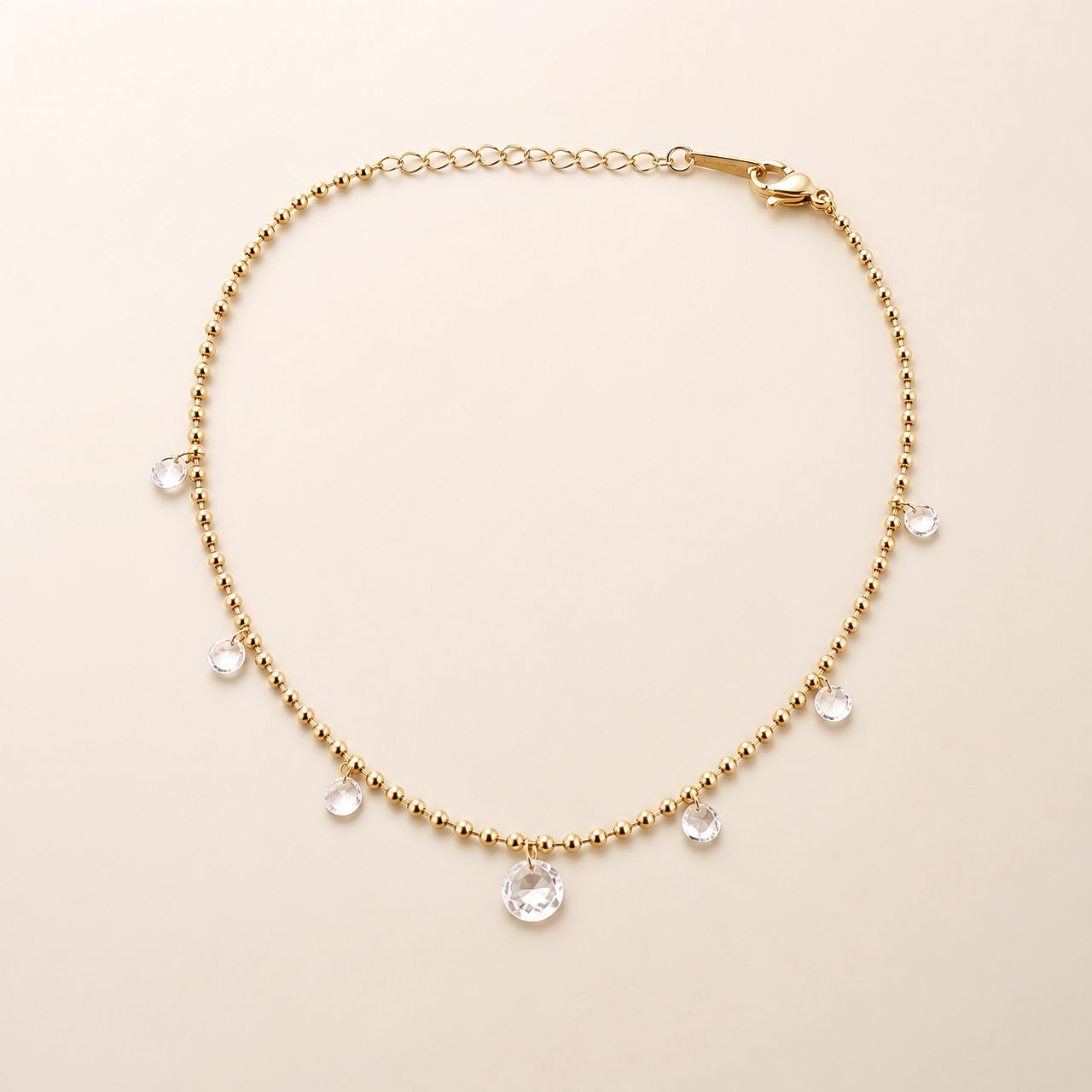 One anklet only: a single flexible yellow-gold-tone polished chain in a fine small-ball/bead construction, with one short oval-cable-link extender section and one visible working lobster-claw closure; no terminal tag is clearly resolved. The main chain run is approximately 30 times the width of the largest dangling component, and the extender is roughly one-eighth of the main chain length.