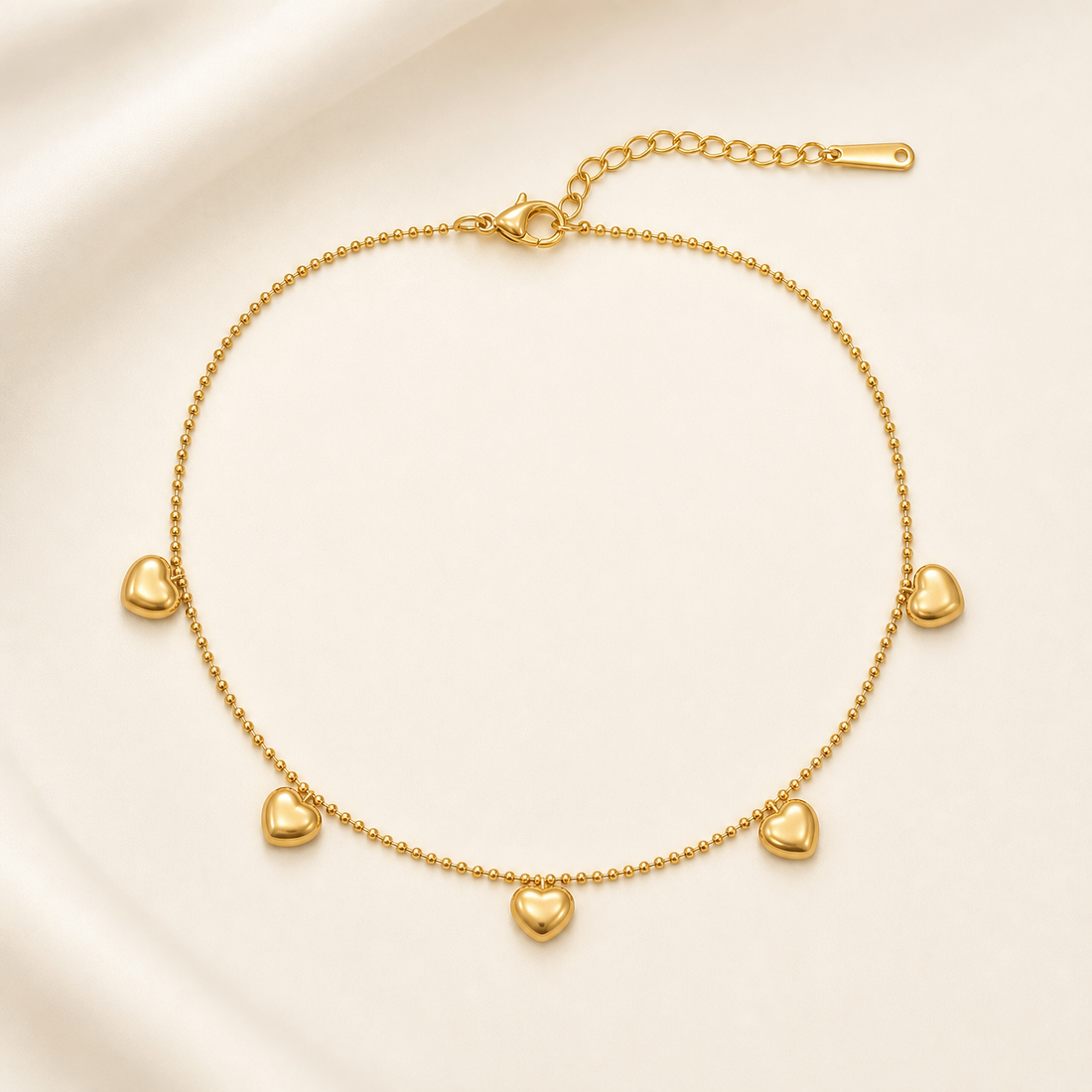 One anklet in yellow-gold-tone metal with a polished finish. It is a single-strand, fine-gauge ball chain (small round bead links) forming one closed loop with no branches. The chain run measures roughly 30–35 times the width of its largest component, and the curb-link extender chain is about one quarter the length of the main chain. A working lobster clasp is present.