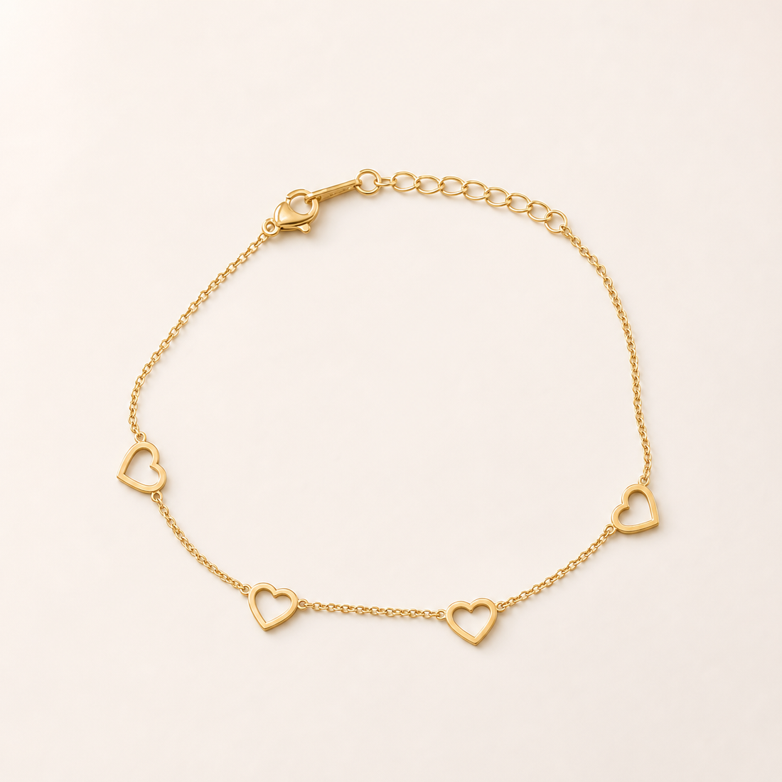 One anklet in yellow-gold-toned metal with a polished finish. It is a single-strand, fine-gauge cable chain of small oval links, unbranched, with one working lobster-claw clasp and a short extender of larger oval links ending in a plain terminal ring. The main chain run is roughly 25 times the width of the largest component (a heart motif), and the extender is about one fifth of the main chain length.