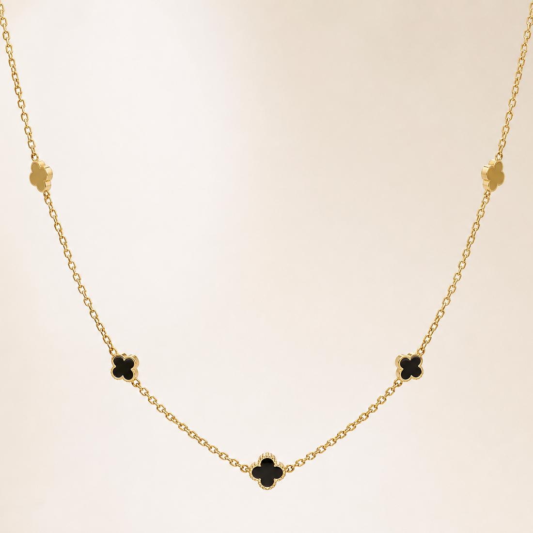 Single station necklace of yellow-gold tone with a polished finish, built as one fine cable chain of small oval links carrying fixed four-leaf clover (quatrefoil) motifs threaded directly onto the chain run rather than dangling. The chain run is approximately 60 times the width of the largest clover motif; no extender chain is visible in the field and the closure is partly obscured, with no working clasp clearly resolvable.