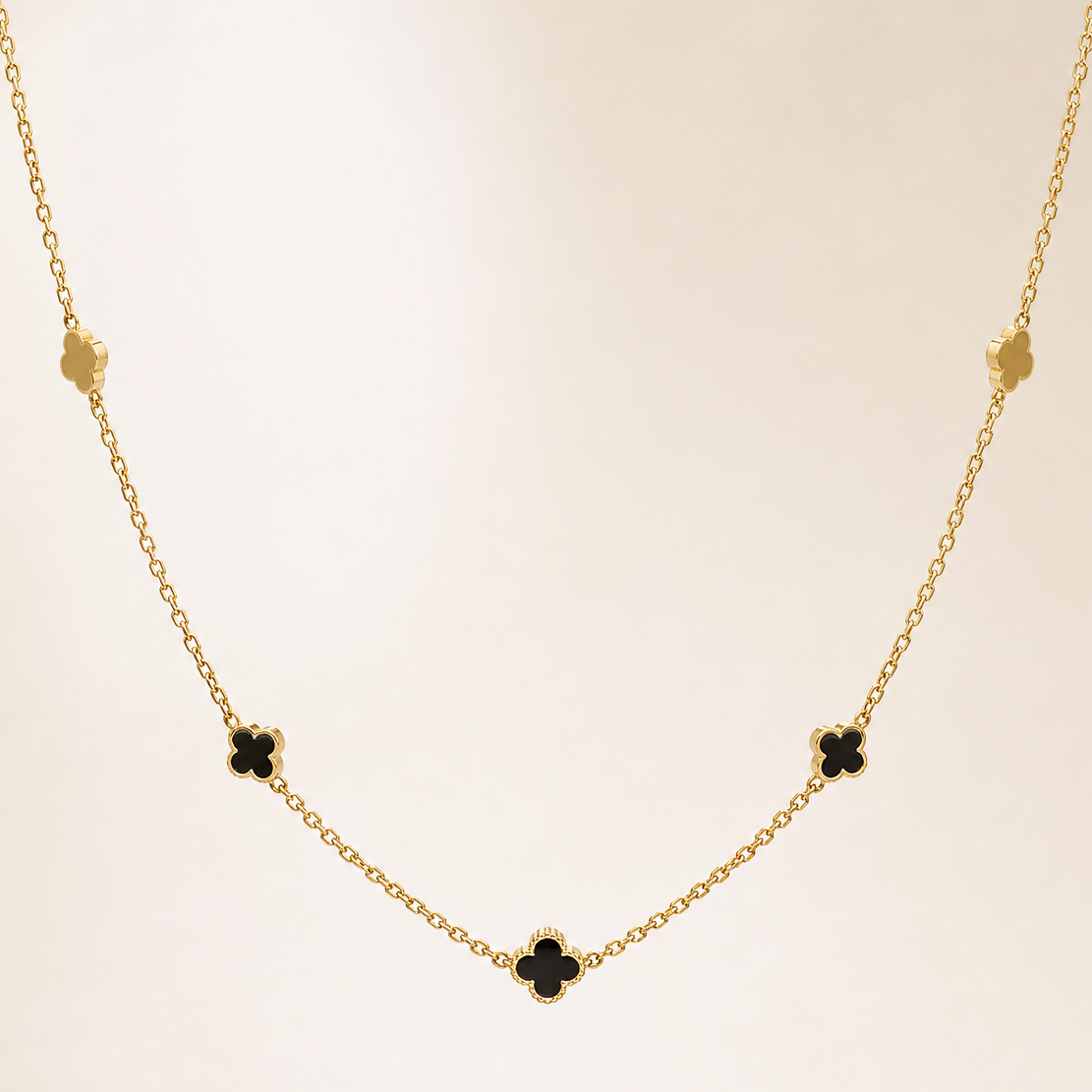Single station necklace of yellow-gold tone with a polished finish, built as one fine cable chain of small oval links carrying fixed four-leaf clover (quatrefoil) motifs threaded directly onto the chain run rather than dangling. The chain run is approximately 60 times the width of the largest clover motif; no extender chain is visible in the field and the closure is partly obscured, with no working clasp clearly resolvable.