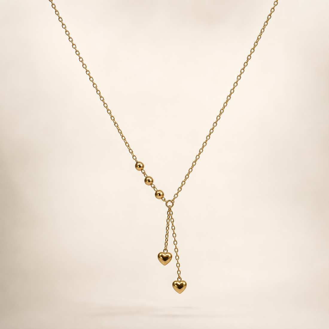 A single necklace in yellow-gold-toned metal with a polished finish. It is one continuous strand of fine, small-gauge oval cable-link chain forming a Y configuration: the main chain run is roughly 80 to 100 times the width of the largest component (the heart charms), and any extender, if present, is not visible.