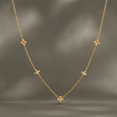One necklace. Yellow-gold metal with a polished finish. Single-strand fine cable chain of small round links, carrying five fixed station motifs spaced along the strand. The chain run is approximately 35 times the width of the largest (central) component; the clasp and extender area is partly obscured and not clearly visible, so extender length cannot be confirmed, and no working closure is resolvable in view.