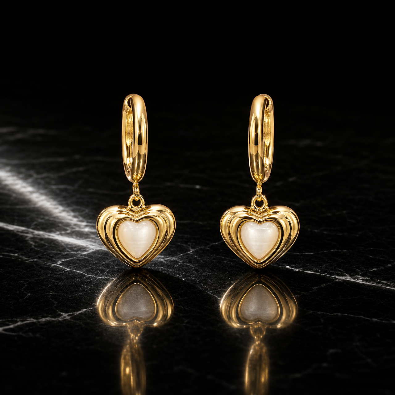 Two earrings, one pair, in polished gold-toned metal with a reflective finish. Each has a small huggie-hinge hoop fitting of short length and standard gauge; the total drop is approximately twice the widest part. Three articulated sections hang from one another: the hoop, a small connector link that hinges freely, and a heart dangle.