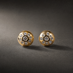 Two ear-worn stud earrings of one design. Each is a polished yellow-gold domed disc, round in outline, its surface flush-set with clear round faceted stones: one larger central stone surrounded by smaller graduated stones scattered across the dome, all in smooth bezel-style recessed settings; exact stone count is not fully resolvable. The earrings are rigid, single-section studs with no articulation or dangling parts; overall depth is roughly equal to the disc width.