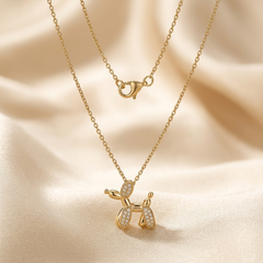 This is a single pendant necklace constructed from yellow-toned metal with a polished finish. The pendant is shaped to resemble a balloon animal dog. The body, head, and tail sections consist of smooth metal, while the ear and leg sections are encrusted with small, clear, round-cut stones set closely together in a pavé style. The pendant is suspended from a fine cable chain that connects to a loop located on the upper back section of the dog figure.