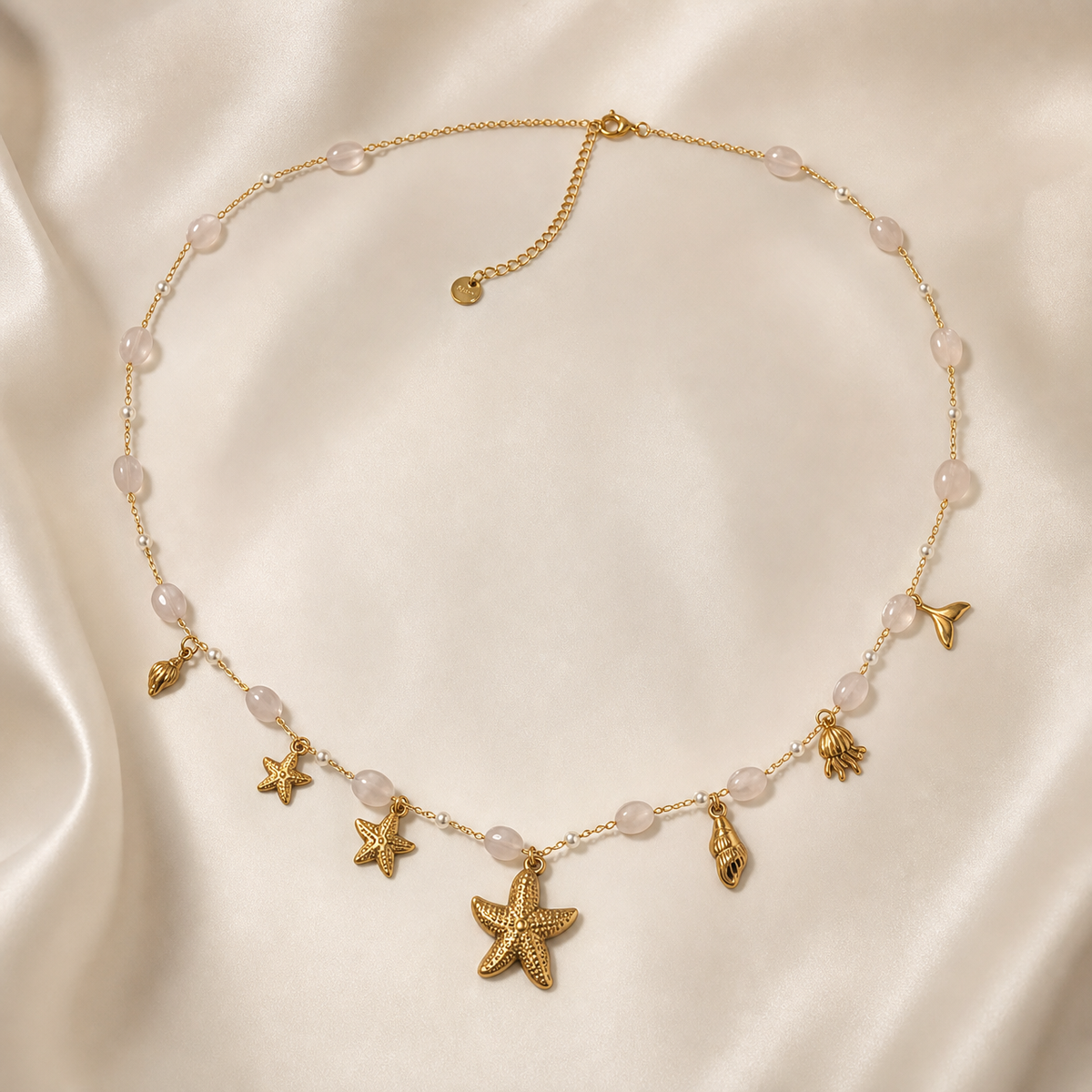 One single-strand gold-tone necklace with a polished finish, laid as an open loop on a fine cable chain of small oval links, interrupted by stations of oval milky pale-pink translucent beads (approximately 15 visible) alternating with tiny round clear spacer beads on short bar connectors.