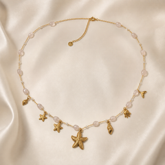 One single-strand gold-tone necklace with a polished finish, laid as an open loop on a fine cable chain of small oval links, interrupted by stations of oval milky pale-pink translucent beads (approximately 15 visible) alternating with tiny round clear spacer beads on short bar connectors.