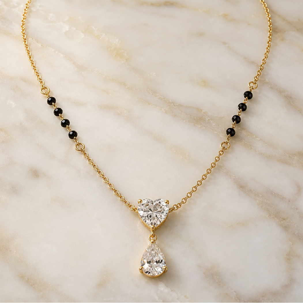 One necklace of yellow-gold-toned metal with a polished finish, built as a single fine-gauge cable chain with small oval links. From each chain end, the sequence runs: plain chain, then a short beaded section of small black barrel-shaped beads threaded onto the gold strand, then a return to plain cable chain continuing to the pendant. Four black beads are resolvable on each side of the strand, eight in total, evenly spaced within each group.