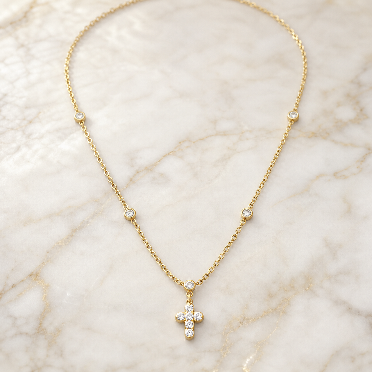 One necklace in yellow gold-toned metal with a polished finish, built as a single fine oval-link cable chain of light gauge. Fixed along the strand at spaced intervals are round bezel-set stations, each a clear colourless faceted stone in a smooth gold-toned bezel; the spacing is irregular, with stations on both sides of the strand and one station sitting directly at the point where the drop begins.