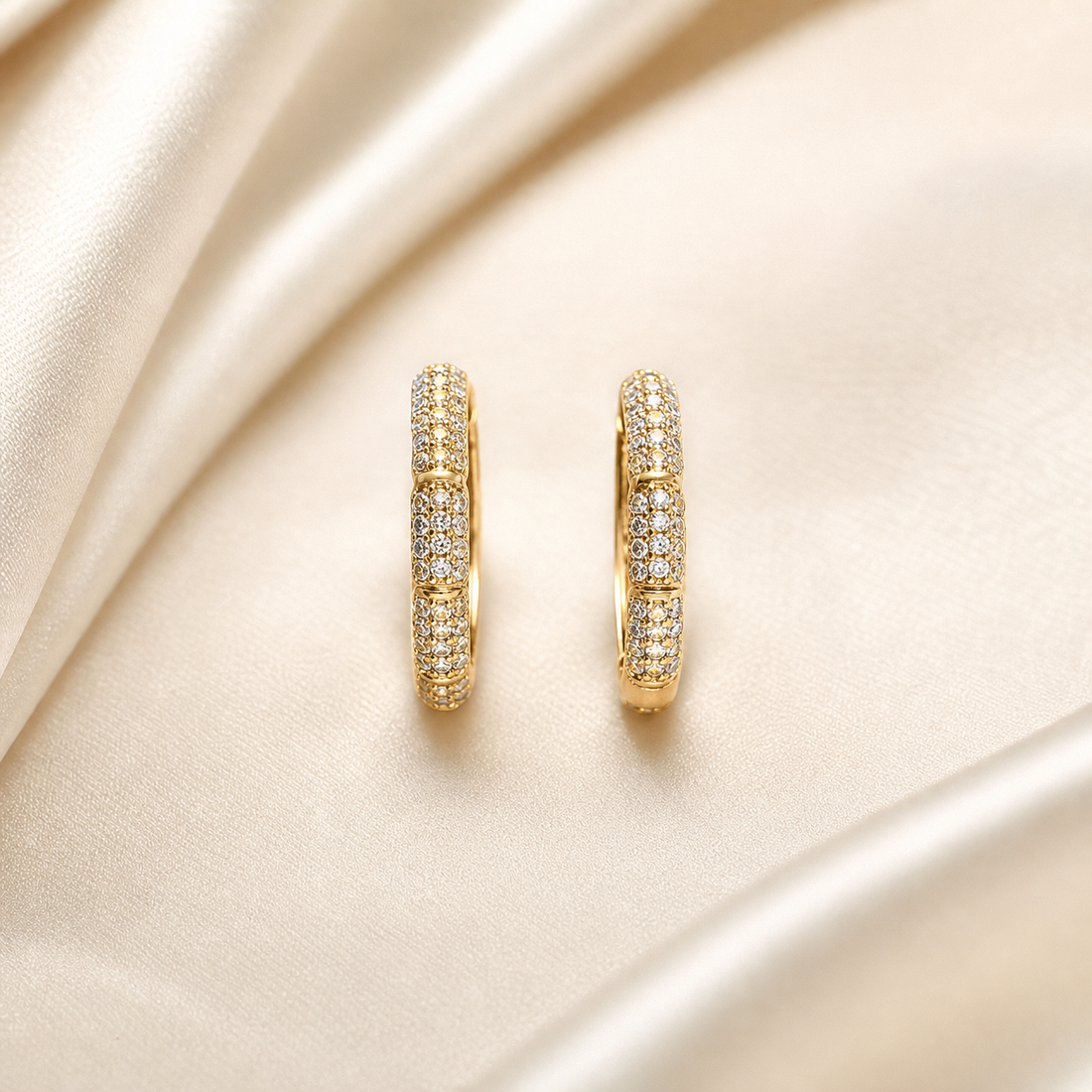 A matched pair of small hinged hoop earrings, two items total. The metal is yellow gold in colour with a bright polished finish. Each earring is a small round-sectioned huggie-style hoop of uniform slim gauge, its outer face continuously set with numerous tiny clear round faceted stones in a pavé-style setting; the individual stones are too small and densely packed to count reliably and form a continuous field rather than separated stations.