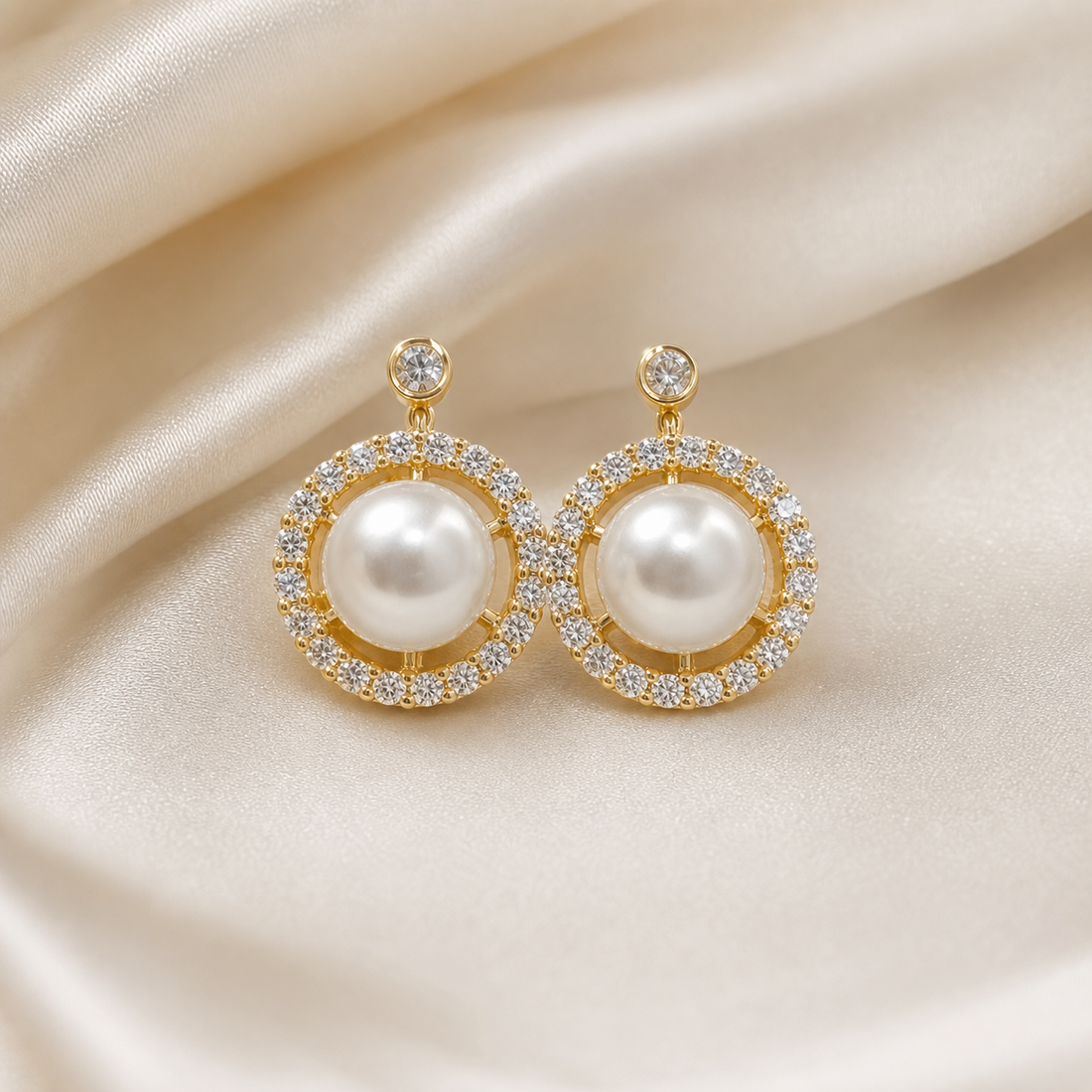 A matched pair of two earrings in yellow-gold-toned metal with a polished finish. Each earring is a fixed circular cluster suspended from a short post: at the top of each is a small round clear faceted stone in a bezel or rim setting, joined by a slim metal link to the main round head below.