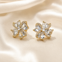 A matched pair of stud earrings, two items, in yellow-gold-tone metal with a bright polished finish. Each earring is a single compact flower-head cluster built from clear faceted stones set in gold-tone mounts. Each flower head is composed of five pear-shaped (teardrop) clear faceted stones arranged radially with their pointed ends meeting at the centre, each stone individually held in a prong-and-rim setting; a continuous halo of small round pavé-set clear stones edges each pear stone along its outer