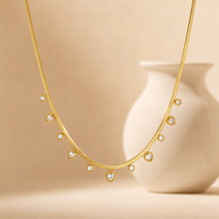 One gold-toned necklace of a single flat snake (herringbone-style) chain, medium gauge, with a smooth flexible ribbon-like surface and polished finish. The chain run is roughly 40 times the width of the largest heart charm; no extender is visible in view, so extender length is indeterminate (the ends and any clasp are partly obscured and not resolvable).