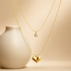 Two separate necklaces, both yellow-gold in colour with a bright polished finish, each built as a single strand of fine, round snake chain of slim uniform gauge. Neither strand branches; each is a continuous closed loop of chain carrying one charm. The shorter chain run is roughly thirty times the width of its largest component, the longer roughly fifty times its heart's width; no extender chain or terminal tag is visible on either piece, and no working clasp is visible on either strand, so closure type