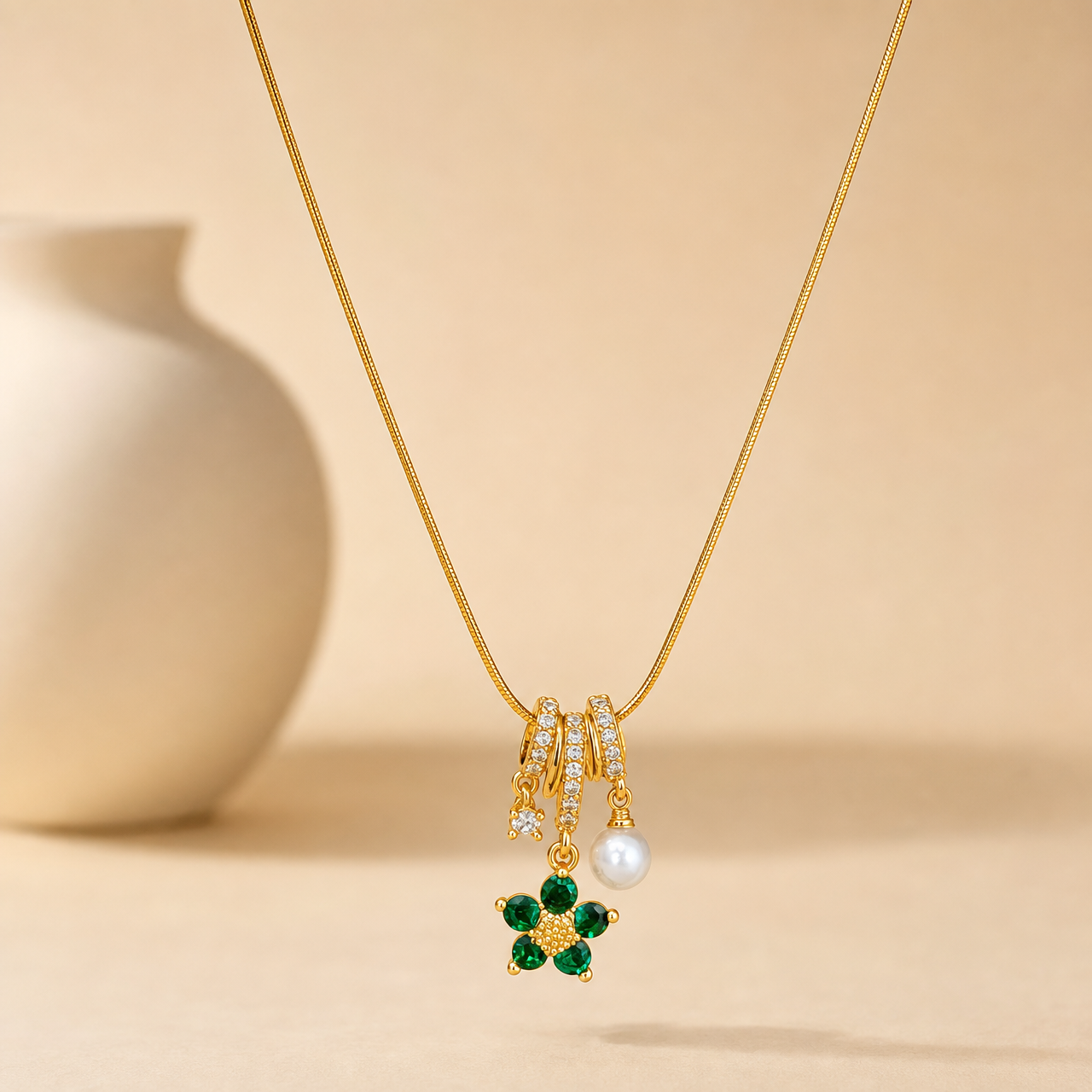 A single gold-tone pendant necklace with a polished finish. Construction is one continuous strand of fine snake chain, roughly 30 times the width of the largest component, with no visible extender; the closure is not visible in this view. The strand runs into a barrel-style pendant bail of stacked gold-tone rings channel-set with rows of small clear faceted stones, from which three jump-ring-mounted dangles hang: one side dangle is a small prong-set clear faceted round stone; the centre dangle is a flower
