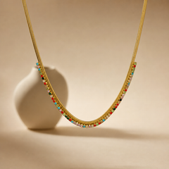 One necklace. Gold-coloured metal with a polished finish, formed as a single flat, flexible woven chain of herringbone/snake type with a fine, tight gauge; no branches, joins or second strand. The visible chain run is roughly 60 to 70 times the width of one stone setting. No extender is visible, so no extender fraction can be stated; the closure is partly obscured and no working clasp, extender chain or terminal tag is resolvable.