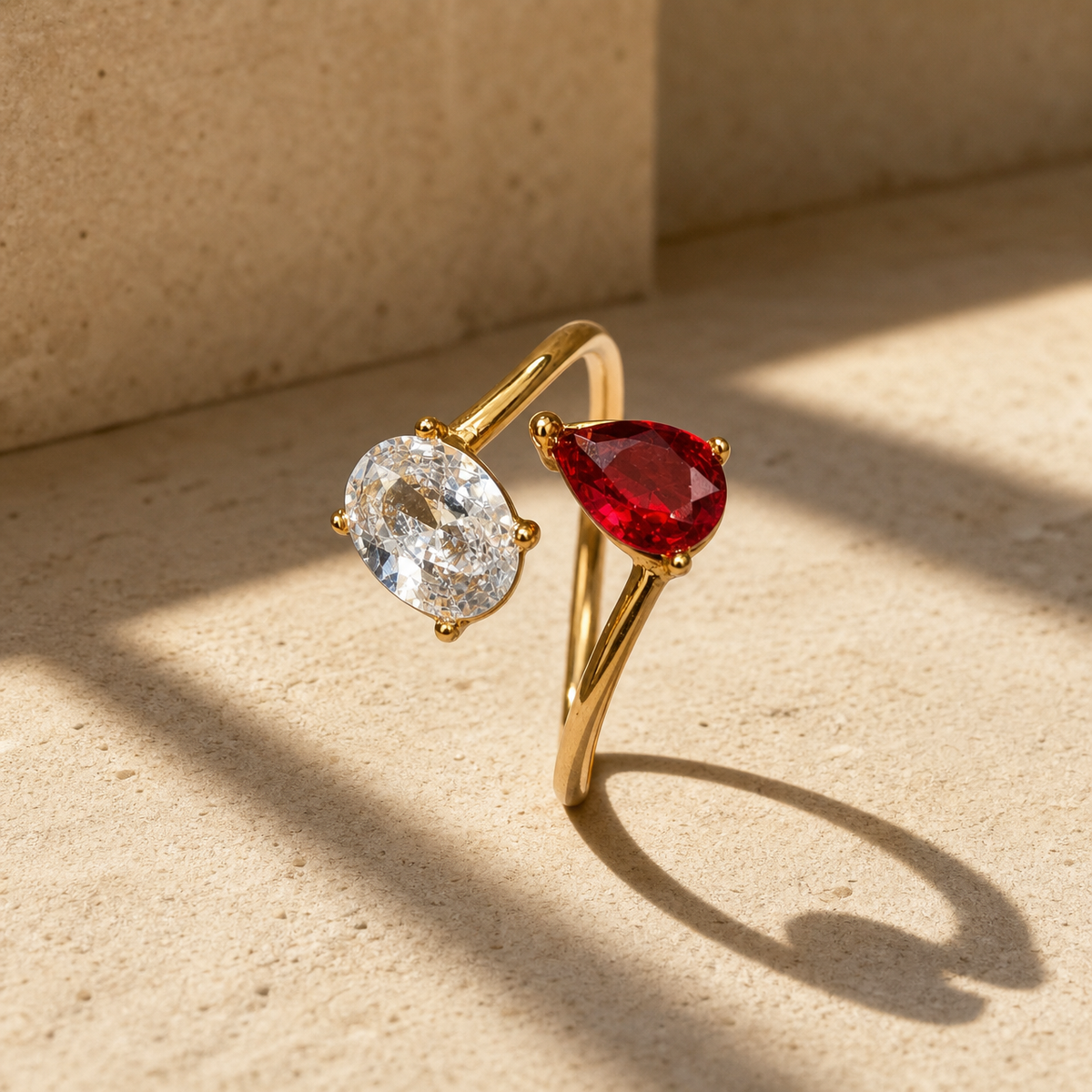One finger-worn ring in polished yellow gold with a rounded, moderately slender band, roughly one-quarter the width of the head, formed as an open adjustable bypass band whose two ends each carry a stone. The head comprises two prong-set faceted stones facing one another: one oval-cut clear colourless stone and one pear-cut red stone of similar size, each held by four rounded prongs. The clear stone shows visible internal inclusions.