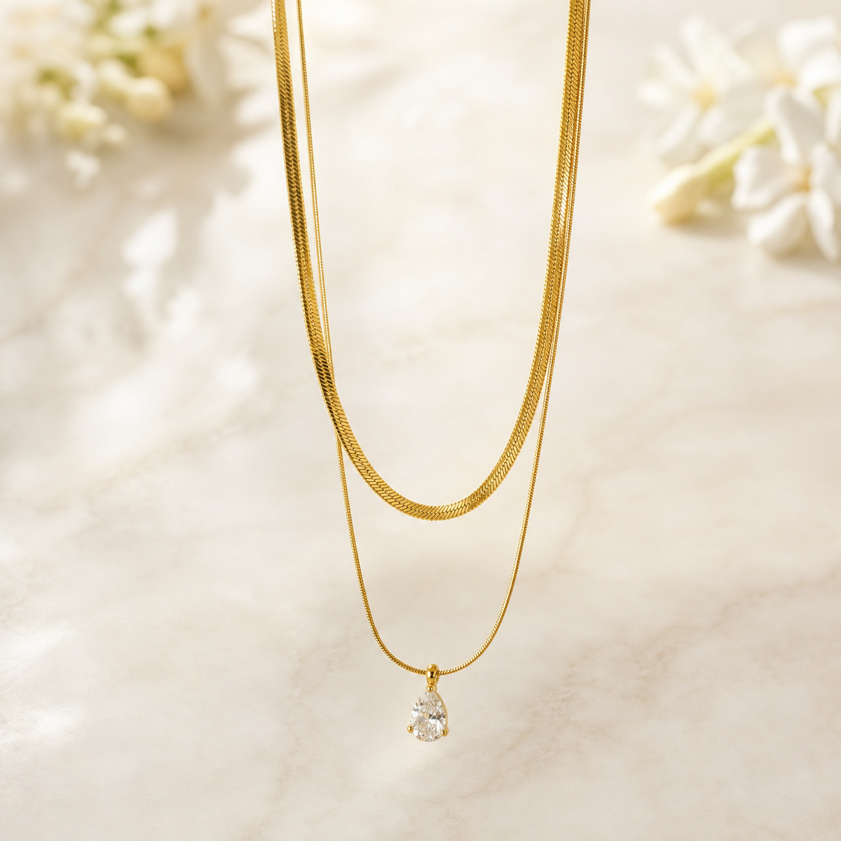One necklace comprising two joined gold-tone strands sharing a single closure area: a wider flat herringbone chain with a bright polished, lightly ridged surface, and a finer round snake chain of noticeably smaller gauge running parallel to it. Yellow-gold colour throughout with a reflective finish. The visible chain run is long, roughly thirty times the width of the largest component; no separate extender segment is resolved, so its length cannot be stated as a fraction.