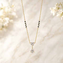 One necklace in yellow-gold-tone metal with a polished finish, built as a single strand of fine curb chain of small, uniform link gauge. Each side of the strand carries a station group of four small cylindrical black beads threaded onto the chain between chain-link spacers, giving eight black beads in total, symmetrically placed partway along the strand. The chain run is approximately twenty-five to thirty times the width of the largest component, the central stone.