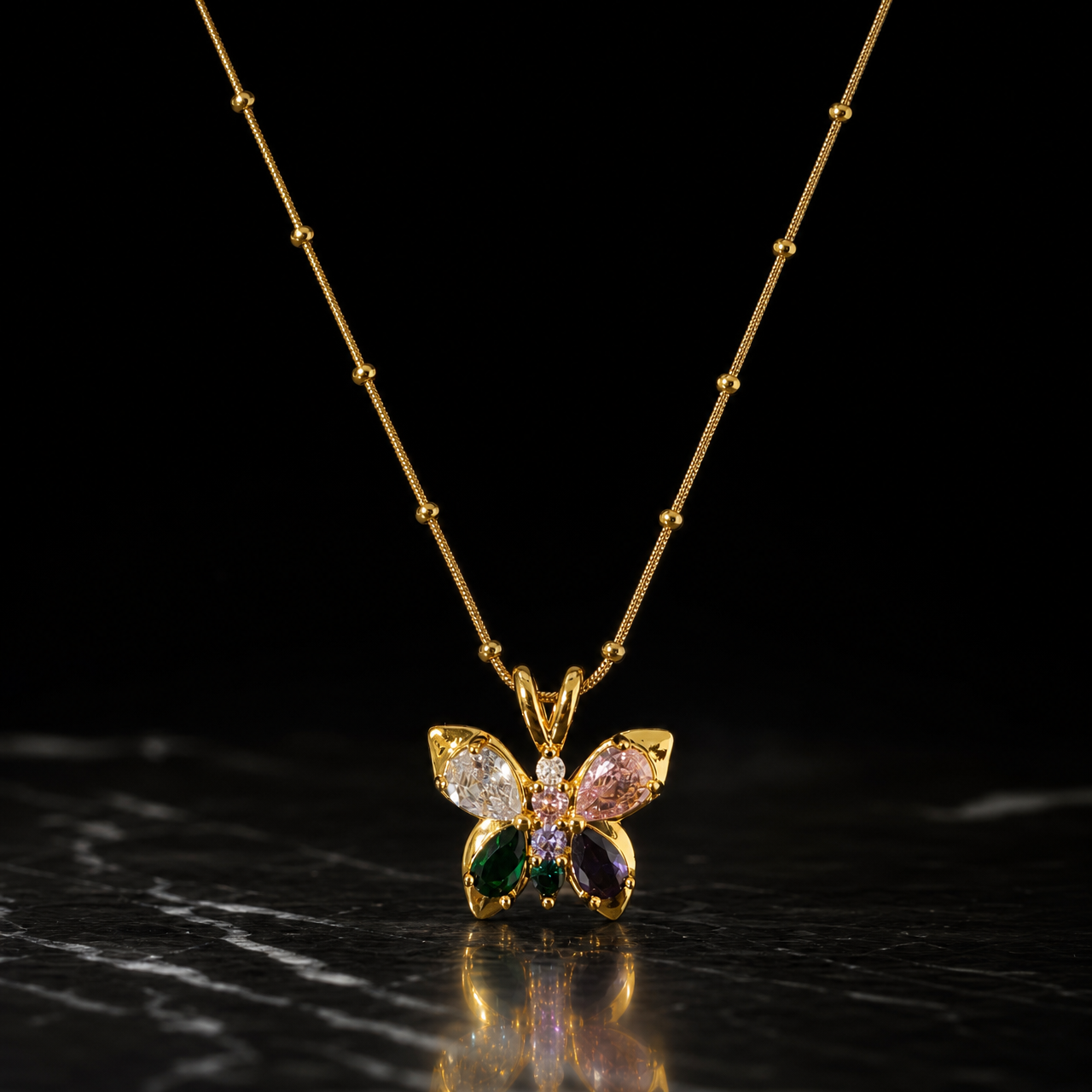 One gold-tone pendant necklace with a polished finish. It is a single fine snake chain studded with small round metal beads at intervals, of fine gauge, carrying one butterfly pendant suspended from a split double-loop bail. The visible chain run is roughly fifteen to twenty times the pendant's width; no clasp, extender or terminal tag is visible, as both chain ends run out of view, so the closure state is unconfirmed and the piece is partly obscured.