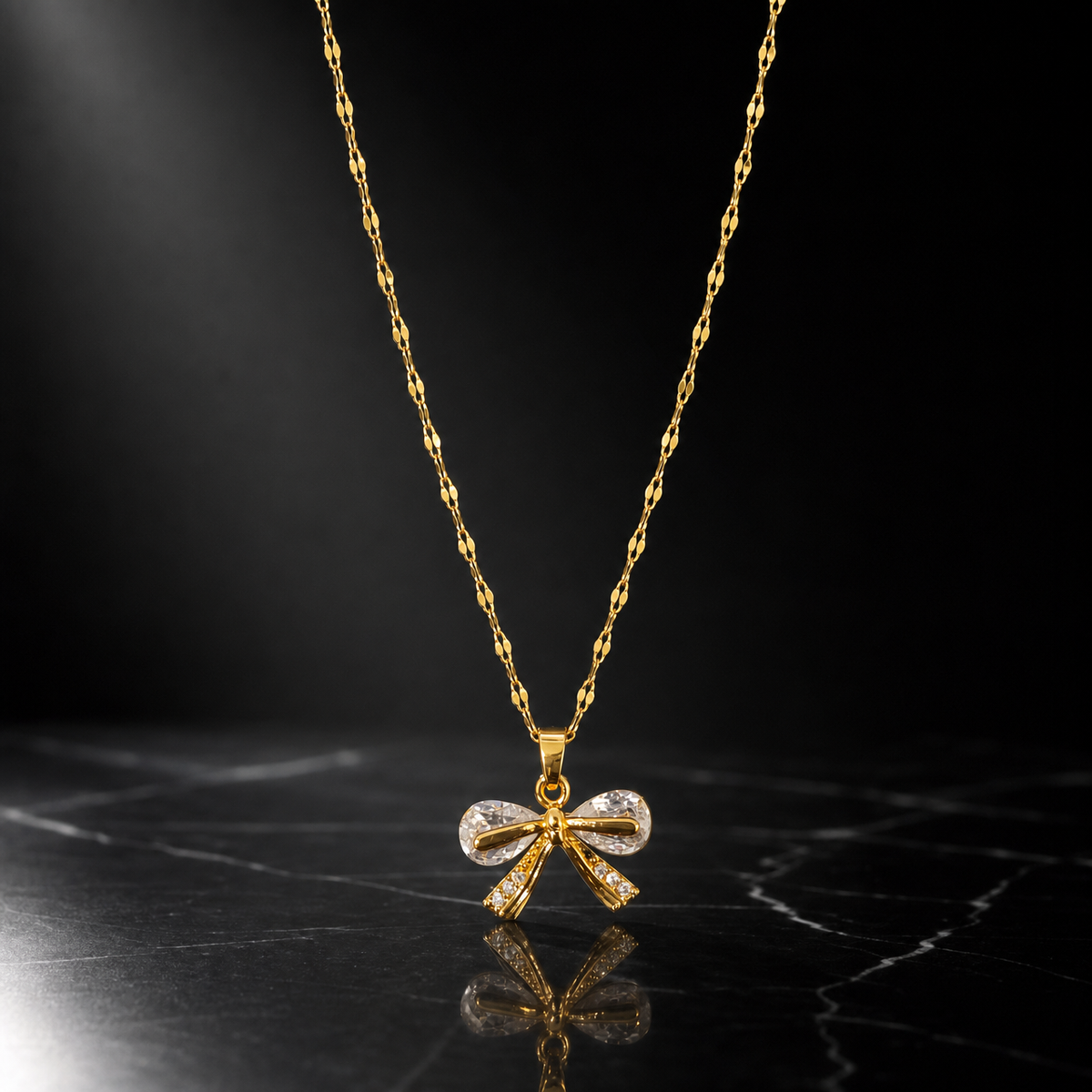 One necklace in yellow gold-tone metal with a polished finish. A single fine strand of flattened, elongated decorative link chain of small gauge carries one dominant bow pendant suspended from a tapered metal bail by a jump ring; the chain ends run off-frame and no clasp, extender or terminal tag is visible, so no working closure can be confirmed. The visible chain run is approximately twenty-five to thirty times the pendant's width.