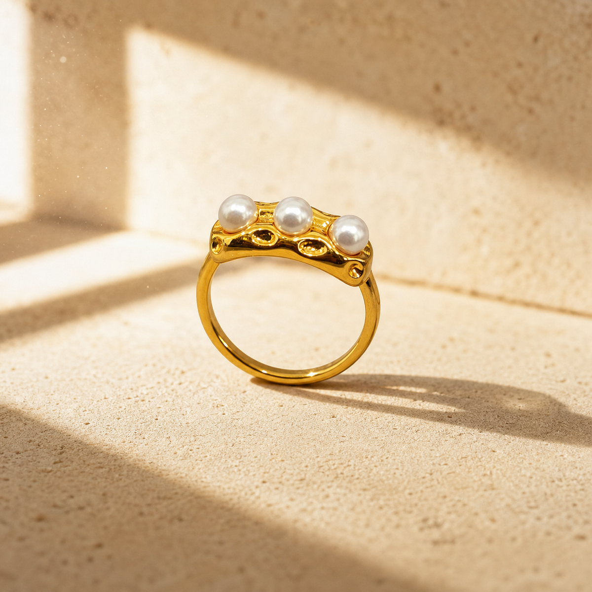 One finger-worn ring in yellow-gold-toned metal with a polished, irregularly textured finish. The band is rounded in profile, a closed circle, roughly one-third the width of the head. The head is an elongated, organically shaped molten-style bar with a lumpy, hand-worked relief and several small recessed dimples across its face. Set into the head are three round white pearls of similar size, each seated in a low bezel-style cup, evenly spaced in a row.