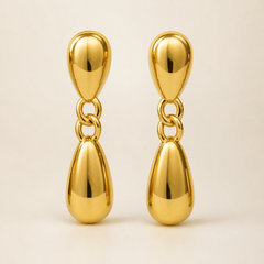 Two ear-worn earrings of one design in yellow-gold-tone metal with a high-polish mirror finish. Each is a drop earring on a post fitting (the posts and backs are partly obscured) emerging from a domed, hollow teardrop stud. From the stud hangs a short articulated chain of two interlocking oval links, ending in a larger solid-metal teardrop dangle, so each earring has three sections hinging at two joints. The total drop is roughly three times the widest teardrop width.