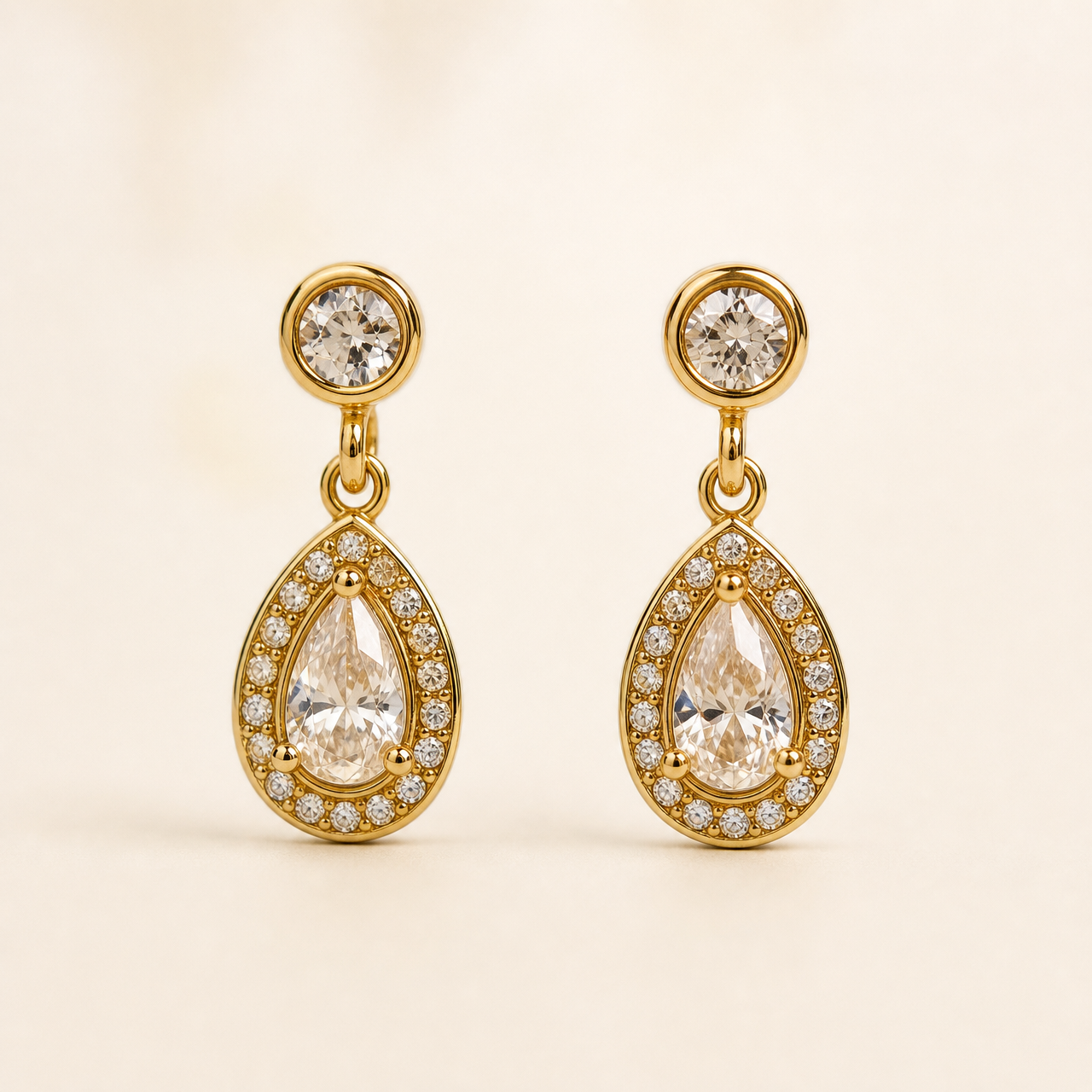 Two ear-worn earrings of one design in yellow-gold-toned metal with a polished finish. Each has a post fitting (back not visible, likely a standard push post), the post topped by a small round clear faceted stone in a smooth bezel. From the stud a short jump-ring link articulates to a teardrop-shaped drop section, giving two hinged sections; overall drop is roughly two and a half times the widest point (the teardrop).