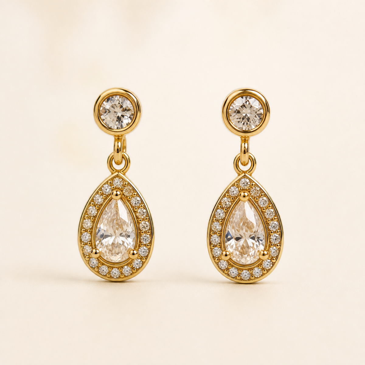 Two ear-worn earrings of one design in yellow-gold-toned metal with a polished finish. Each has a post fitting (back not visible, likely a standard push post), the post topped by a small round clear faceted stone in a smooth bezel. From the stud a short jump-ring link articulates to a teardrop-shaped drop section, giving two hinged sections; overall drop is roughly two and a half times the widest point (the teardrop).