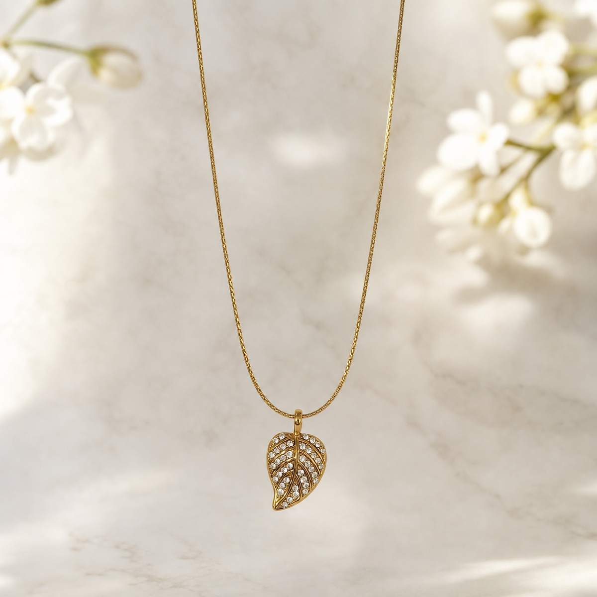 A single pendant necklace. Yellow-gold-tone metal with a polished finish. Construction is one continuous fine-gauge strand, a narrow snake or foxtail-style chain of very small tight links, with no branches and no additional strands. The chain run is approximately 25 to 30 times the width of the largest component, the leaf pendant.