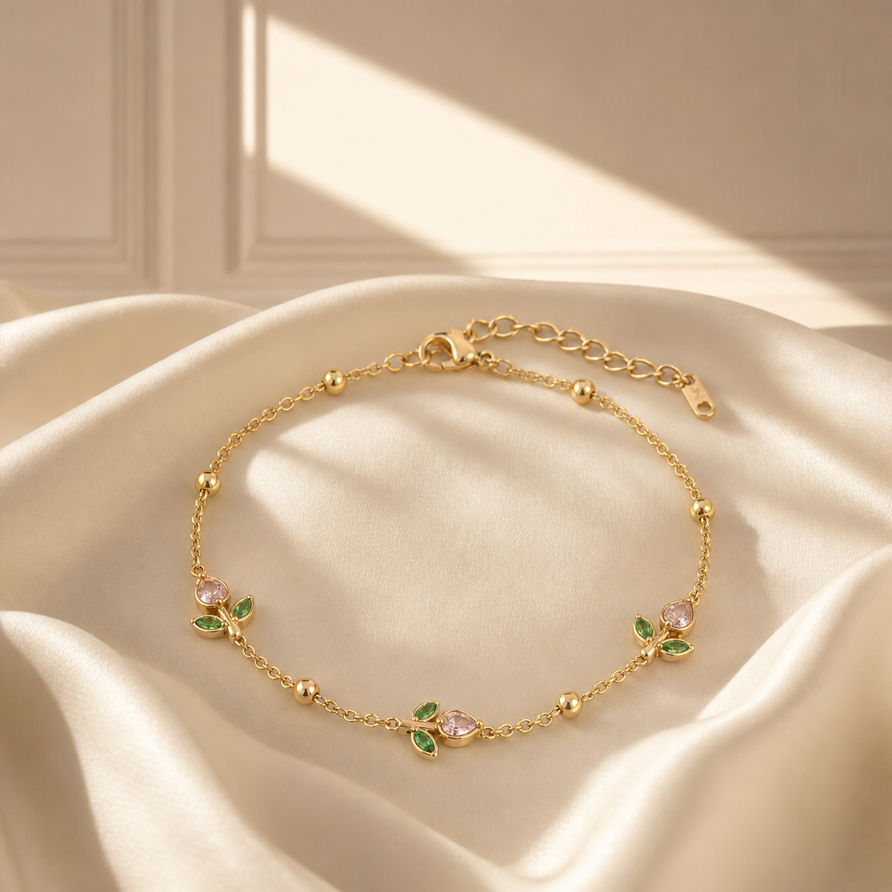 One wrist-worn chain bracelet in yellow-gold-tone metal with a polished finish. It is a single-strand fine cable chain of small oval links, running end to end as one continuous strand interrupted by spaced components; the chain run is roughly 40 to 45 times the width of the largest component (the floral stations), with an extender chain about one-fifth the main chain length ending in a small flat perforated tag. A working lobster clasp is visible, connecting the chain to the extender.