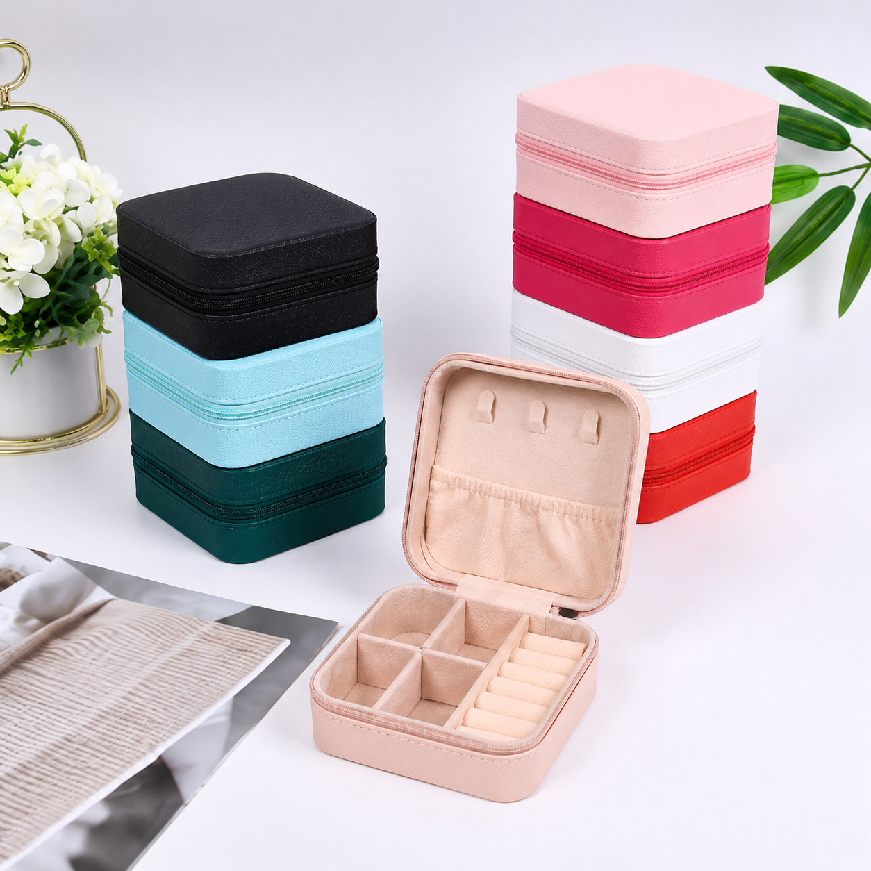 Blush pink zip-closed jewellery travel case open to show compartments, ring slots and earring holder, with stacked cases in other colours behind