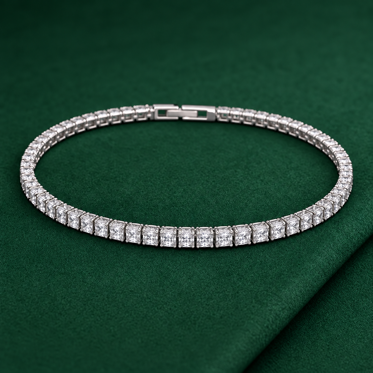 Silver-tone brass tennis bracelet with square-cut clear stones in a line setting and a box clasp, shown lying flat on a green cloth, second view