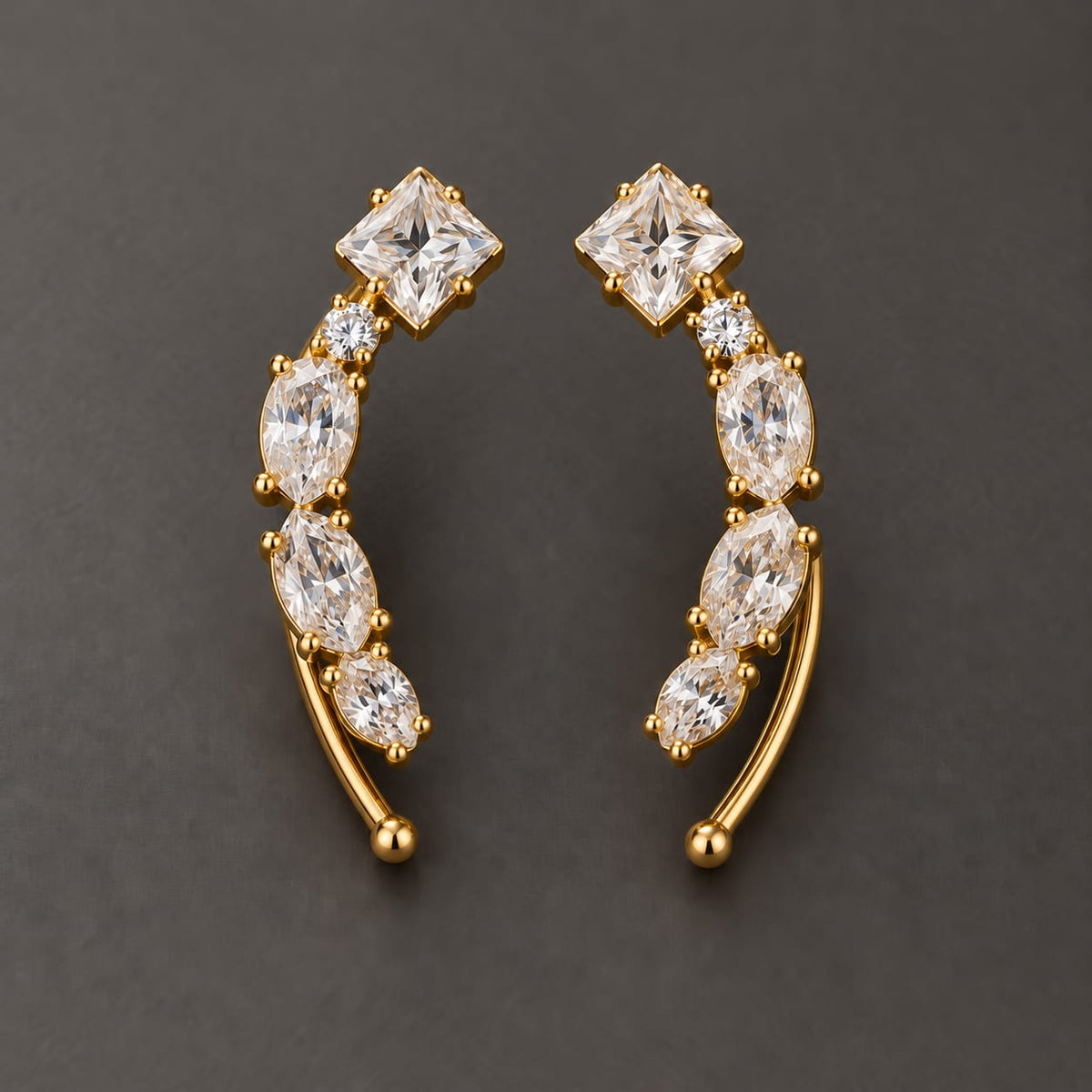 Gold-tone brass climber earrings with a curved row of clear princess and marquise cut stones and a round stone, worn as a pair