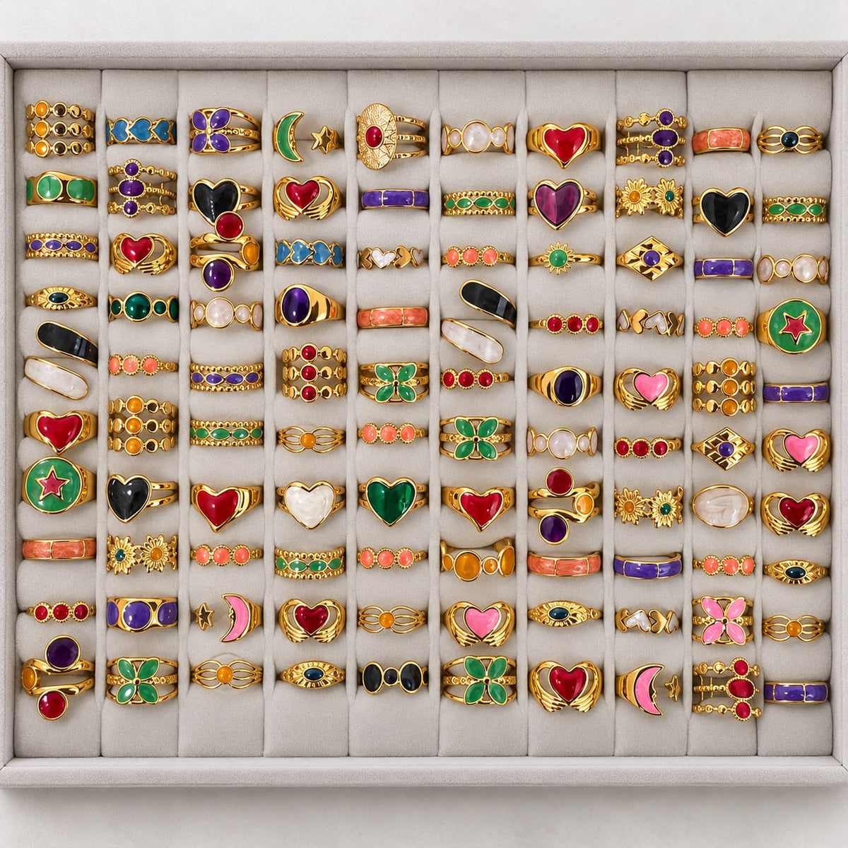 Gold-tone 304 stainless steel rings in a set of 50 with enamel hearts, stars and moons, and coloured stones, arranged in a grid tray