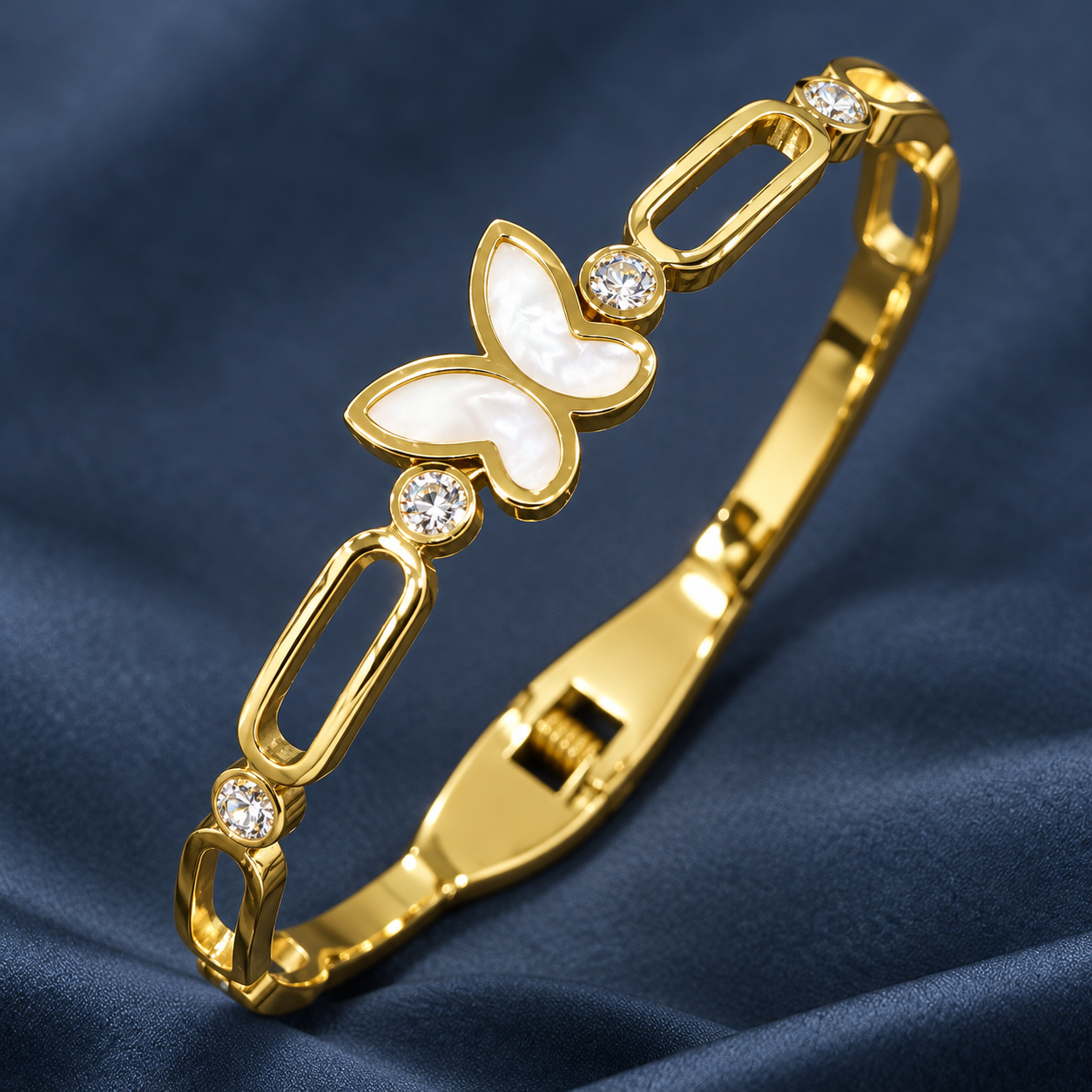 Gold-tone 304 stainless steel bangle bracelet with open oval links, a white shell butterfly and round crystals, shown on a dark blue fabric
