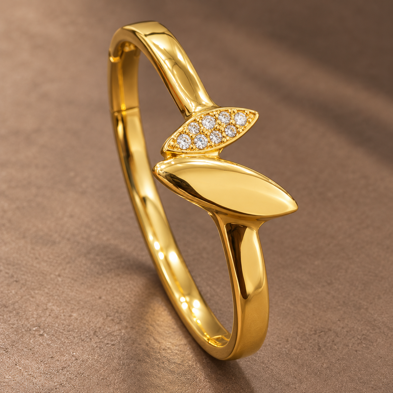 Gold-tone 304 stainless steel kada bracelet with a polished leaf motif and a row of clear stones on the upper leaf, shown from an angle