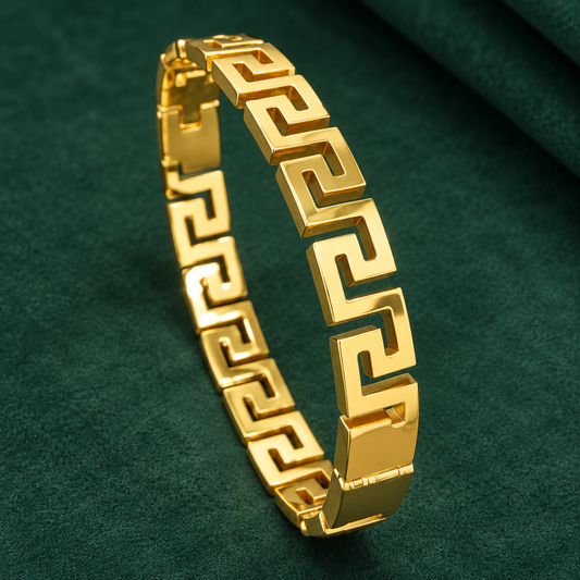 Gold-tone 304 stainless steel bracelet with a Greek key meander link pattern and a hinged clasp, lying on a dark green surface