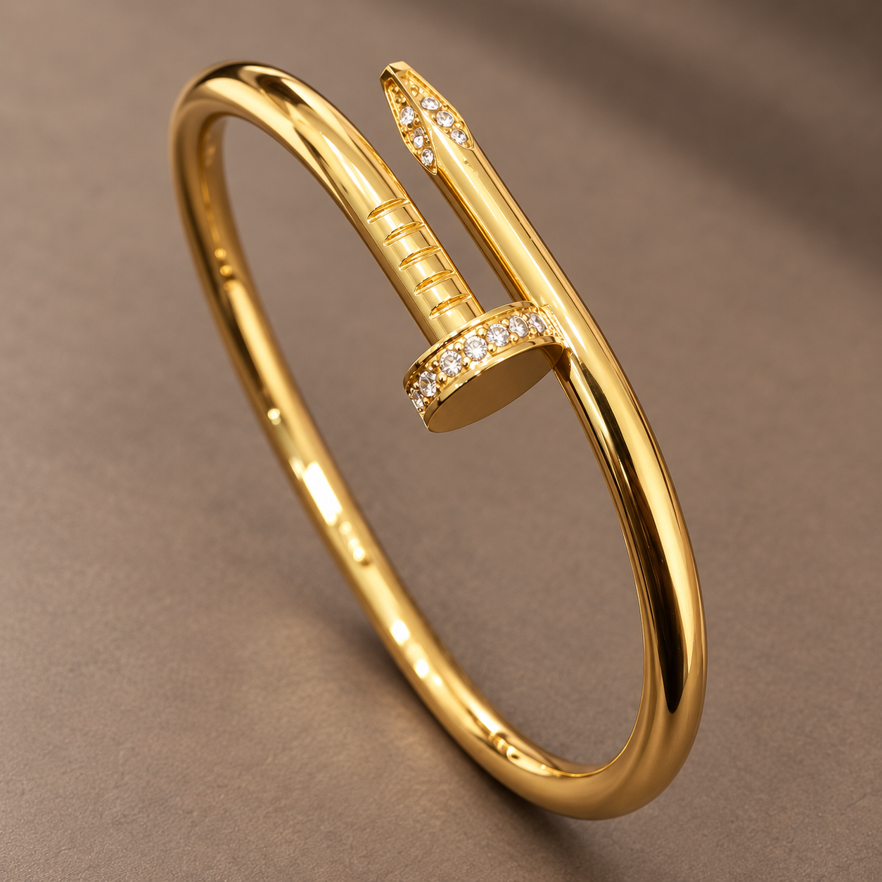 Gold-tone 304 stainless steel bangle with a nail-shaped clasp set with crystals, shown on a flat surface