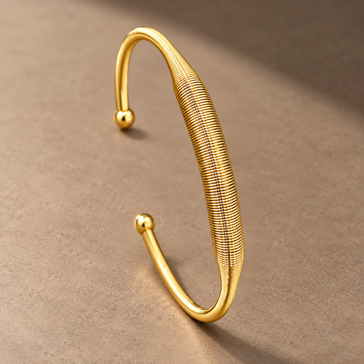 Gold-tone 304 stainless steel open cuff bracelet with a ribbed coil band and ball-tipped ends, on a flat surface
