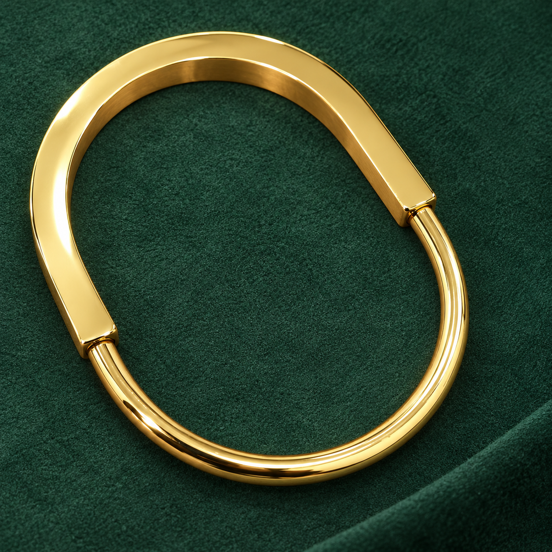 Gold-tone 316L stainless steel hinged kada bracelet with a flat wide front band and a round tube back, shown on a green suede surface